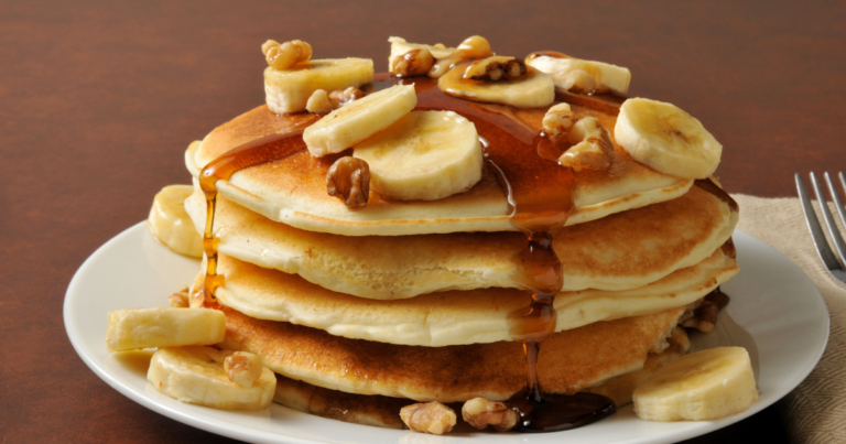 panquecas de bana, com fatias pequenas fatias de bananas em cima da panqueca, acompanhada de calda de caramelo